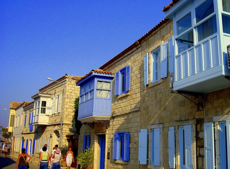 Steinhäuser mit blauen Holzbalkonen und Fensterläden in Alaçatı