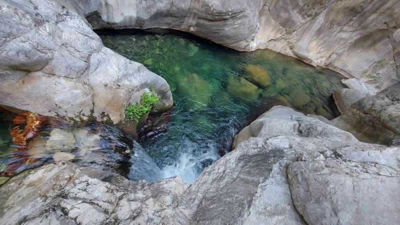 A small waterfall pouring into a clear green pool between pale rocks in Sapadere Canyon
